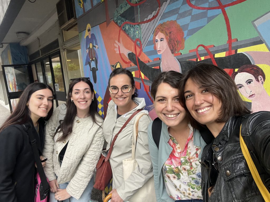 Foto di gruppo delle project manager del progetto Freedom, sono 5 giovani donne castane e sorridenti.
Lo sfondo è un murales colorato